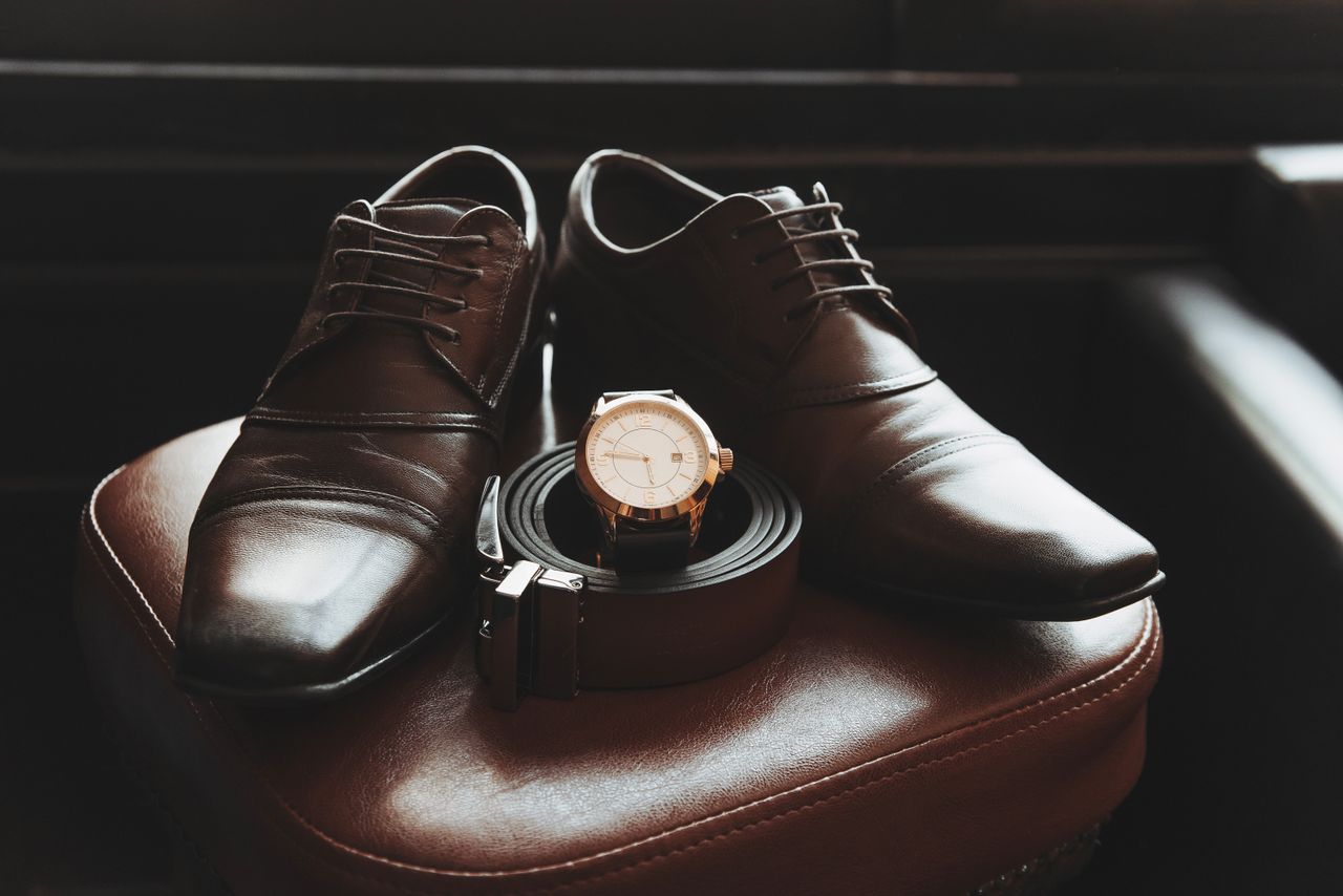 services-01 Close-up of stylish men's shoes, belt, and wristwatch on a leather chair, showcasing elegance and fashion.