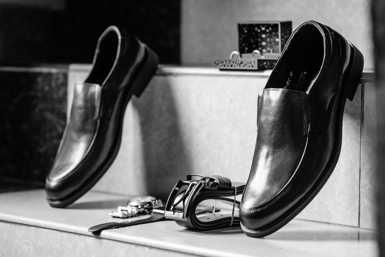 services-02 Stylish black leather formal shoes paired with accessories in a black and white setting.